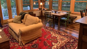 A cozy room with a wooden ceiling, a dining table with chairs, a sofa, and a large window with a view of trees. - LAKESIDE RETREAT!  A HIDDEN GEM!!! (Ossipee)
