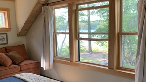A bedroom with a large window, a bed, a wooden ceiling, and a view of trees and a lake. - LAKESIDE RETREAT!  A HIDDEN GEM!!! (Ossipee)