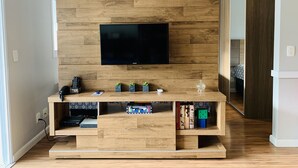 A modern living room with a flat-screen TV mounted on a wooden wall, a wooden entertainment unit below, and a sliding glass door leading to another room. - Akile Carlos Sampaio (São Paulo)