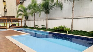A rectangular swimming pool with blue tiles, surrounded by a wooden deck and palm trees. - Akile Carlos Sampaio (São Paulo)