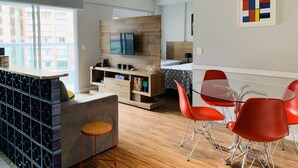 A modern living room with a TV, wooden furniture, a dining area with red chairs, and a view of buildings outside. - Akile Carlos Sampaio (São Paulo)