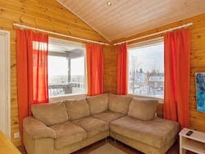 Un sofá de esquina en una habitación de madera con dos ventanas y cortinas rojas.