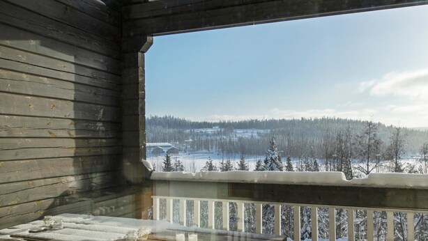 Une cabane en bois dotée d’un balcon donnant sur un paysage enneigé.
