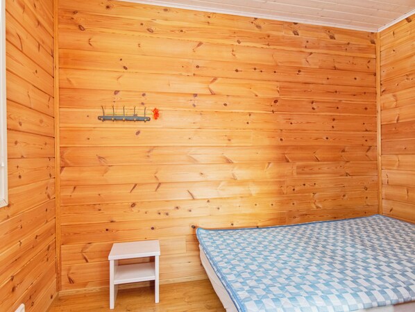 Una habitación con paneles de madera, una cama, una mesita pequeña y un perchero con una flor.
