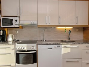 Una cocina con gabinetes blancos, microondas, estufa, lavavajillas y fregadero.