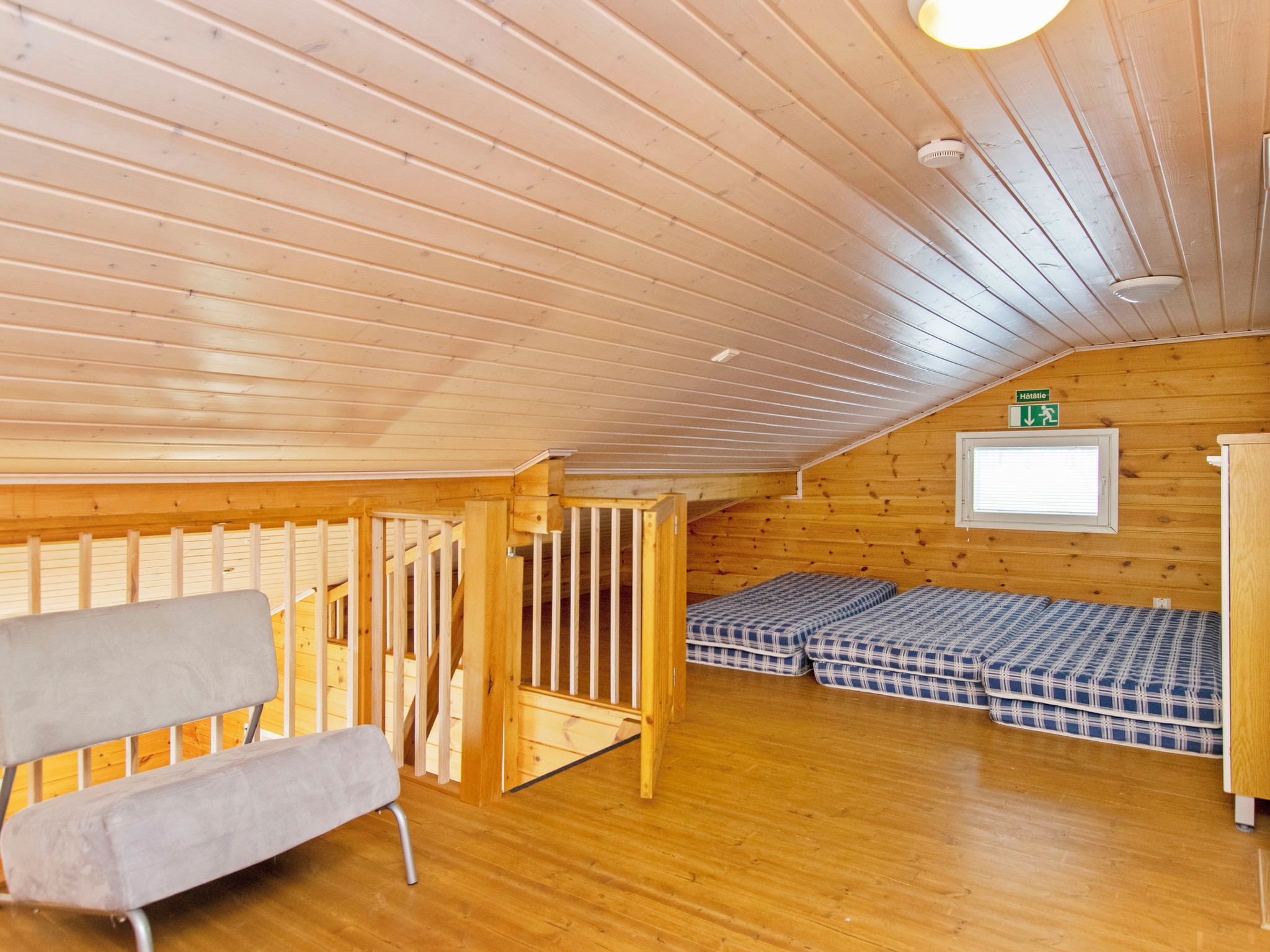 Interior de madera con techo alto, una escalera, una cama y un banco.