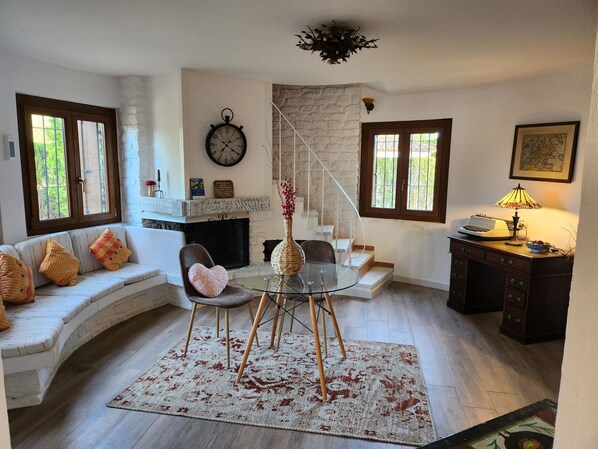 A cozy living room with a fireplace, a sofa, a glass table, and a desk with a lamp.