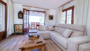 A living room with a beige sofa, a wooden coffee table, and a dining area with a table and chairs. - Hercaris by Interhome (Begur)