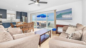 A living room with a ceiling fan, a kitchen with dark cabinets, a dining area, and a large sliding glass door leading to a balcony with a beach view. - Spectacular Ocean Views at Affordable Prices | Super Central | Walk to Everything! (Newport Beach)