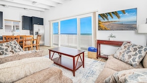 A living room with a sofa, coffee table, and a painting of a beach. - Spectacular Ocean Views at Affordable Prices | Super Central | Walk to Everything! (Newport Beach)