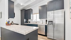 A modern kitchen with dark cabinets, a stainless steel refrigerator, and a marble countertop.