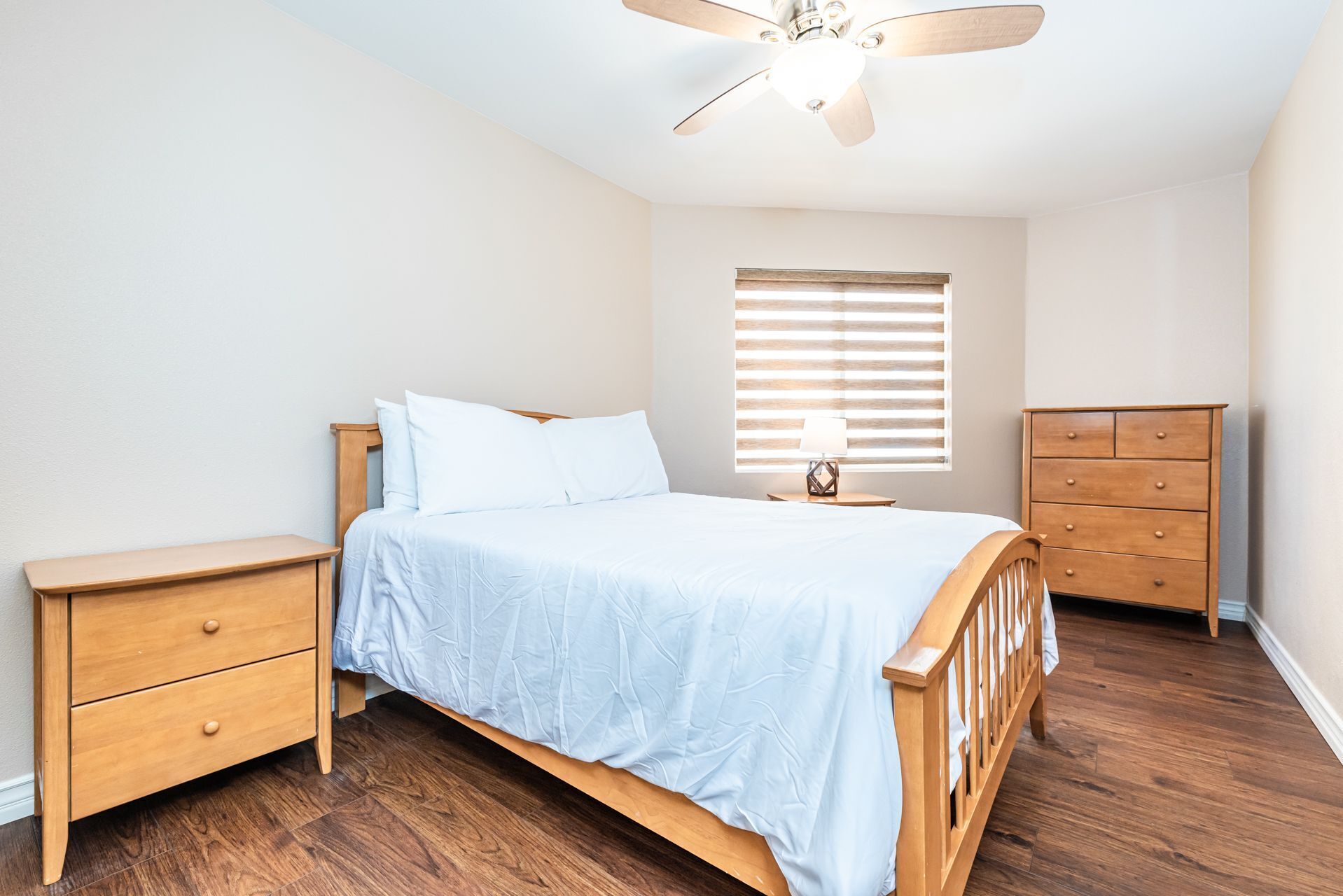 Un dormitorio con cama de madera, mesita de noche, cómoda y ventilador de techo.