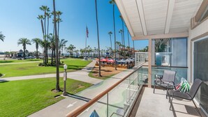 A balcony with a glass railing overlooking a beach with palm trees and a clear sky.