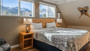 Un dormitorio con una cama grande, dos lámparas de noche, una mesita de noche de madera y vistas a montañas a través de amplios ventanales.