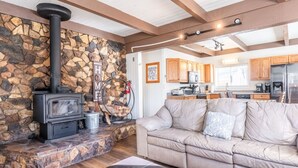 Un salón acogedor con chimenea de piedra, un sofá y una zona de cocina con armarios de madera y electrodomésticos.