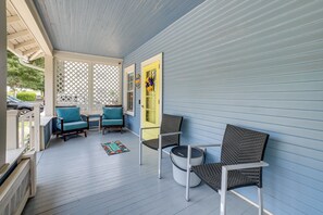 Eine Veranda mit blauer Holzverkleidung, zwei blaue Stühle, ein runder Tisch und eine gelbe Tür.