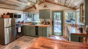 Una cocina con vigas de madera en el techo, armarios verdes, un refrigerador de acero inoxidable y encimera de madera.