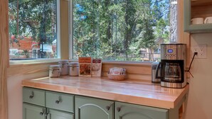 Una cocina con vistas por la ventana, una cafetera y una cesta de revistas.