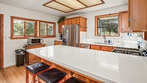 A kitchen with wooden cabinets, a stainless steel refrigerator, a microwave, and a large island with bar stools.