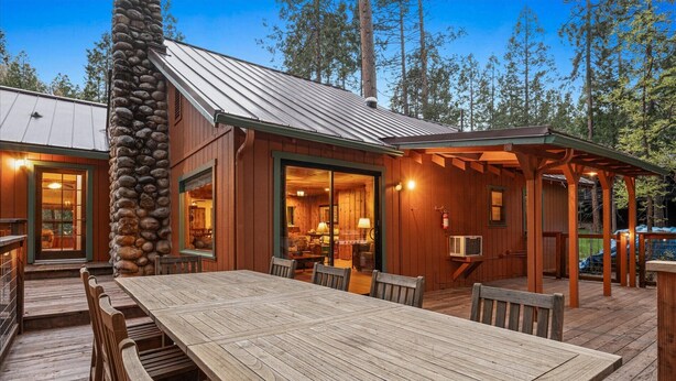 A wooden cabin with a stone chimney, a dining area with a table and chairs, and a covered outdoor seating area.