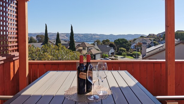 A wooden deck with a table set for two, overlooking a residential area with houses and hills. - 2800sqft Luxurious home with bay view private pool near SF & NAPA (Vallejo)