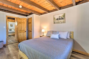 A bedroom with a wooden ceiling, a bed with a patterned bedspread, a nightstand with a lamp, and a painting on the wall. - Lake Escape In the Poconos (Pocono Lake)