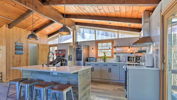 A modern kitchen with wooden beams, a large island with stools, and a view of the snowy landscape. - Lake Escape In the Poconos (Pocono Lake)