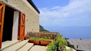 Un edificio de piedra con contraventanas de madera, un balcón con plantas en macetas y vistas al mar.