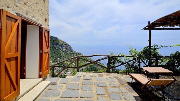 Un patio empedrado de piedra con un banco de madera, una puerta de madera rústica y vistas a un paisaje montañoso.