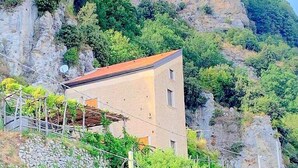 Un edificio con techo inclinado, rodeado de vegetación y terreno rocoso.
