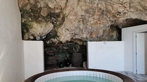 Una bañera de hidromasaje circular con revestimiento de mimbre, frente a un fondo de pared de piedra.