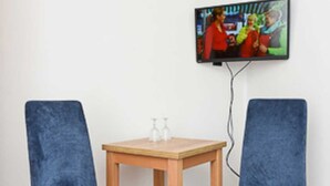A room with two blue chairs, a wooden table, and a TV mounted on the wall. - Double room C - Huus an't Deep in Altharlingersiel (Neuharlingersiel)