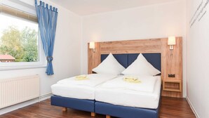 A double bed with a wooden headboard and two bedside tables, a window with curtains, and a radiator. - Double room C - Huus an't Deep in Altharlingersiel (Neuharlingersiel)