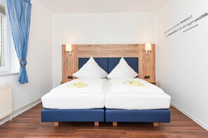 En dubbelsäng med en sänggavel i trä, två sänglampor och en blå accentvägg.