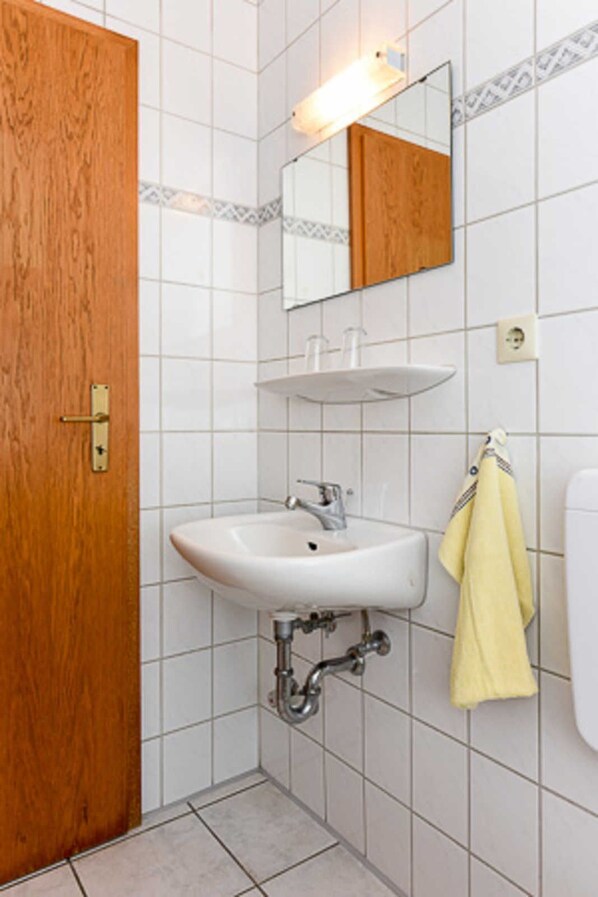 Une salle de bain avec une porte en bois, un lavabo blanc avec un miroir au-dessus, et une serviette jaune accrochée au mur.