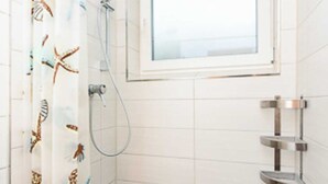 A small bathroom with a shower, a window, and a tiled floor.