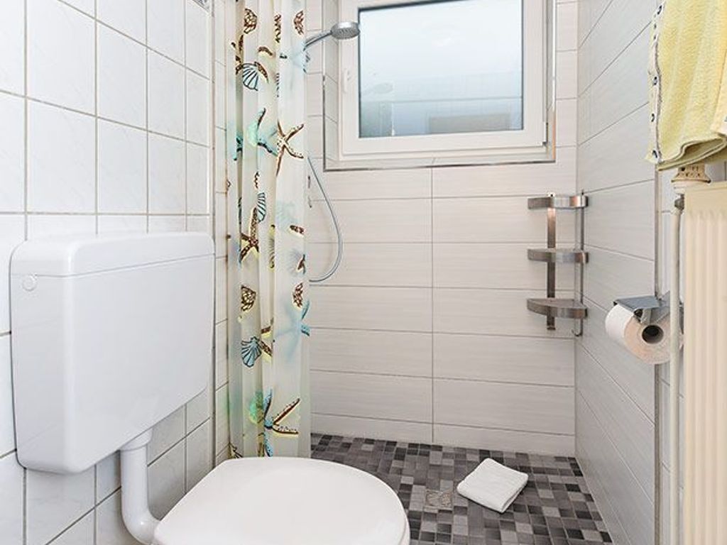 A small bathroom with a toilet, a shower, and a window.