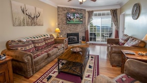 A living room with a fireplace, a ceiling fan, and a large window with curtains.
