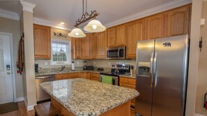 A kitchen with wooden cabinets, granite countertops, stainless steel appliances, and a large island with bar stools.