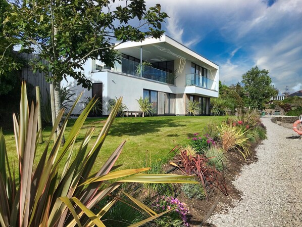 A modern two-story house with a flat roof, large windows, and a well-maintained lawn. - Ancarva - Contemporary Waterside Holiday Retreat (Torpoint)