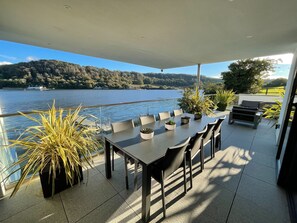Eine Terrasse mit Tisch und Stühlen, Topfpflanzen und Blick auf einen See und Hügel.