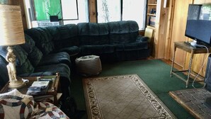 A living room with a dark blue sofa, a patterned rug, a small round ottoman, a television on a wooden stand, and a bookshelf with books and decorative items. - Sunset on the Ottawa "Cottage"- shallow, silky sandy beach w/ 78-84 F warm water (Pembroke)