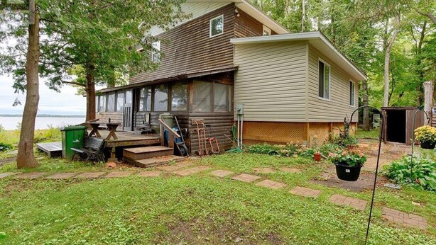 A log cabin with a porch, a small garden, and a view of the water. - Sunset on the Ottawa "Cottage"- shallow, silky sandy beach w/ 78-84 F warm water (Pembroke)