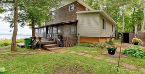 A log cabin with a porch, a small garden, and a view of the water.