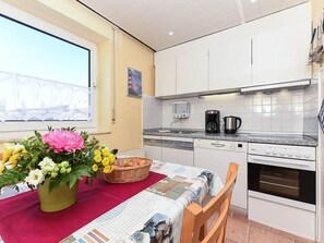 A compact kitchen with white cabinets, a coffee maker, a kettle, and a dining table with a red tablecloth. - Ferienhaus Windmühle (Esens)