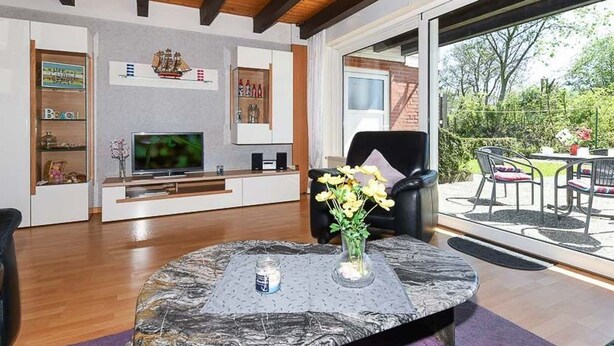 Ein modernes Wohnzimmer mit Fernseher, Couchtisch und Essbereich mit Sitzgelegenheiten im Freien.