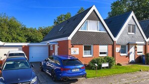 Ein Wohngebäude mit Garage, zwei parkenden Autos und blauem Himmel.