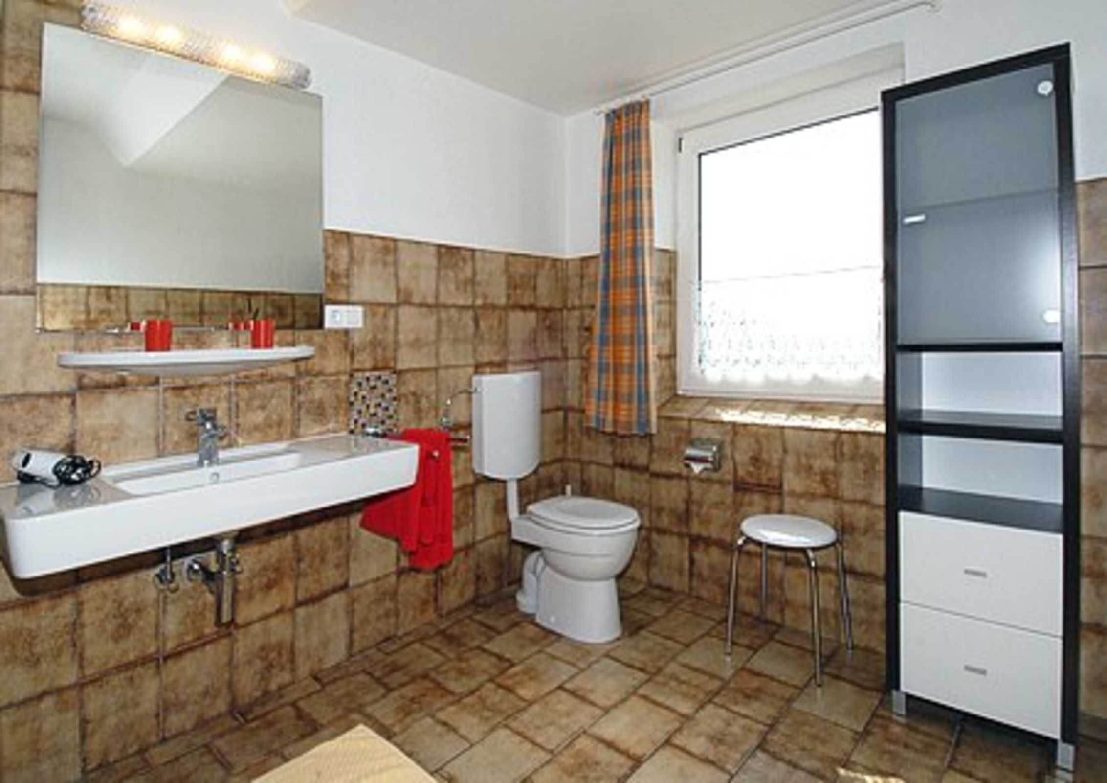 A bathroom with a white sink, mirror, toilet, and a small stool.