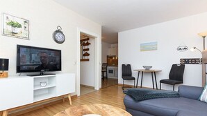 Ein modernes Wohnzimmer mit Fernseher, einer Couch, einem Couchtisch und einem Essbereich mit Stühlen.