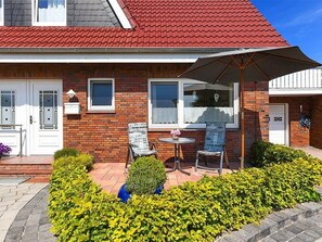 A house with a red roof, brick exterior, and a patio with two chairs and a table.